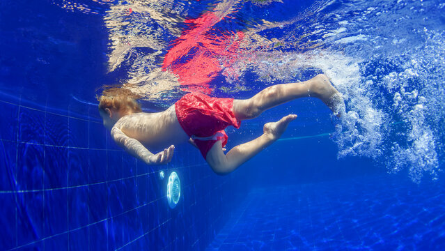 Underwater shot of happy smiling young child jumping with splashes and diving with fun in blue swimming pool. Healthy family lifestyle, water sport activity, swimming lessons on holidays with kids - Powered by Adobe