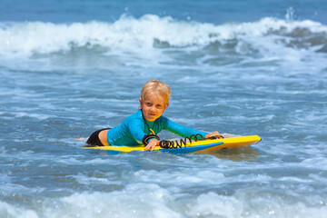 Happy young surfer boy with bodyboard have fun on beach, riding on small ocean waves. Summer adventures, active families, parents and kids lifestyle, sports activities on school holiday with kids
