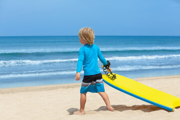 Portrait of little surfer boy with bodyboard have fun on beach, walk by white sand beach. Summer adventures, active families, parents and kids lifestyle, sports activities on school holiday with kids