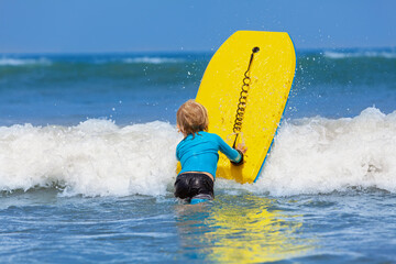 Happy young surfer boy with bodyboard have fun on beach, riding on small ocean waves. Summer adventures, active families, parents and kids lifestyle, sports activities on school holiday with kids