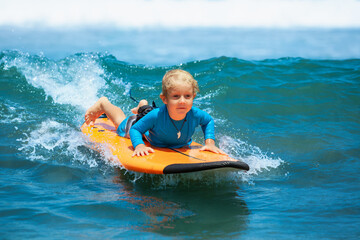 Happy young surfer boy with surfboard have fun on beach, riding on small ocean waves. Summer adventures, active families, parents and kids lifestyle, sports activities on school holiday with kids