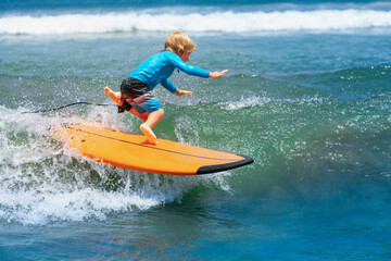 Happy young surfer boy with surfboard have fun on beach, riding on small ocean waves. Summer adventures, active families, parents and kids lifestyle, sports activities on school holiday with kids