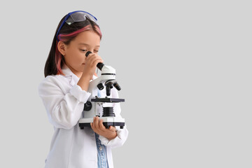 Cute little girl using microscope on grey background