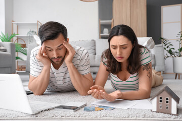 Young couple lying on floor and counting coins at home. Bankruptcy concept