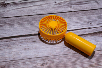 A fan on a wooden background. Portable hand fan. Yellow cooler on a table. Wooden texture background and mini fan