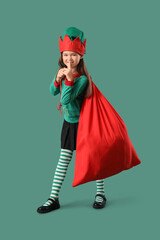 Little girl in elf costume with Santa bag on green background