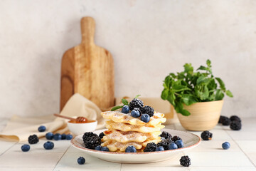 Delicious Belgian waffles with blueberries, blackberries and sugar powder on plate on table against white background