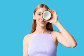 Obraz premium Beautiful young happy woman in stylish summer outfit with half of coconut on blue background