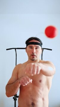 male doing reflex ball exercises, practicing rapid punch coordination with tethered ball at home, focused male athlete engaging in precise reflex ball drills during rigorous home workout
