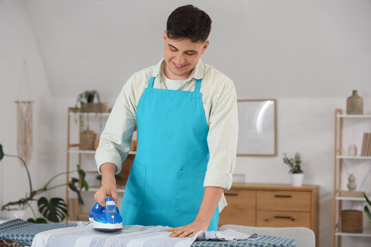 Handsome young happy man ironing clothes on board at home