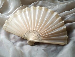 An exquisite cream-colored hand fan displayed on a silken, off-white fabric backdrop
