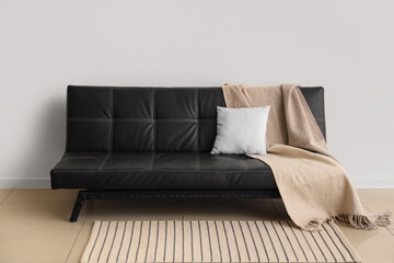 Stylish modern black sofa with pillow and plaid near white wall