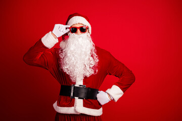 Santa in red costume with hat and beard posing with glasses on a vibrant red background for Christmas themed stock photo