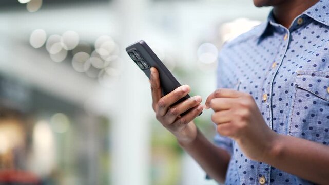 Close up of african american female hand using mobile phone standing in shopping center mall or supermarket. Black woman use online app store for discount, sale promotions on smartphone. light bokeh