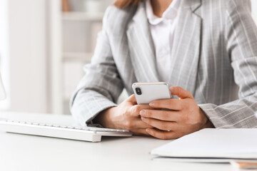 Young businesswoman using mobile phone at table in office, closeup