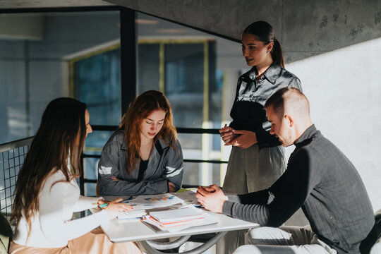A diverse group of colleagues gathers around a table, reviewing papers and notes during a collaborative work session in a contemporary office.