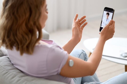 Diabetic young woman with glucose sensor talking to doctor online on sofa at home, closeup - Powered by Adobe