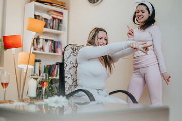 Two cheerful women spend time together indoors, engaging in a lighthearted activity while enjoying their comfy home setting.