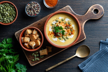 Delicious pumpkin cream soup with baked bread and pumpkin seeds in a ceramic bowl on a wooden table, closeup, top view. Healthy food concert