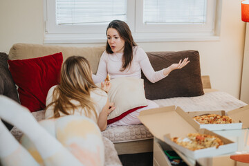 A candid moment of two women talking and enjoying pizza in a living room, showcasing a relaxed and casual home ambiance, with a focus on friendship and leisure time.