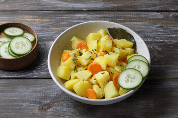 Homemade vegetable stew with potatoes, carrots, and herbs served in a rustic bowl with fresh cucumbers on wooden table. Warm, healthy comfort food with natural colors and soft light