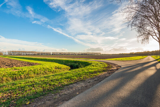 Backlit photograph of an agricultural landscape with ploughed fields, country roads and a ditch.