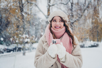 Smiling woman enjoys snowy day outdoors with her smartphone during winter.