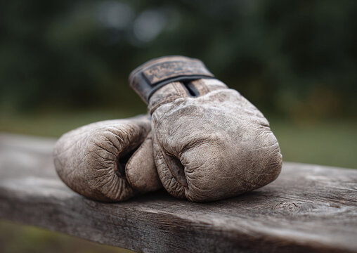 Worn boxing gloves rest on weathered wood, symbolizing resilience, history, and the spirit of combat. Ideal for sports, fitness, or motivational projects.