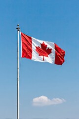 Canadian national flag with red maple leaf flying on tall flagpole in blue sky with single cloud