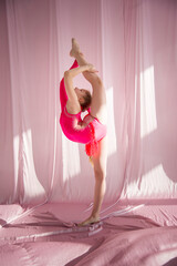 young beautiful flexible gymnast girl in a pink swimming suit posing in studio on white background