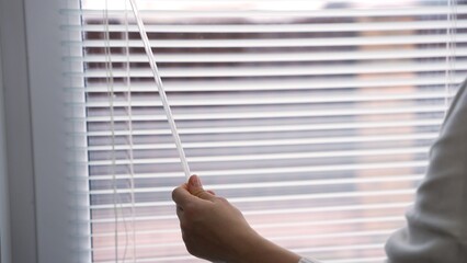 Woman's hand opening and closing window blinds