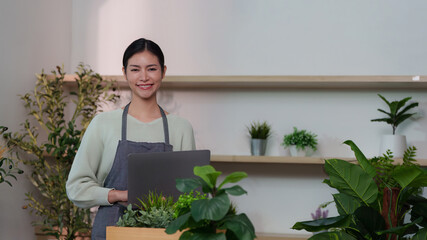 Remote Work. Woman smiling while using a laptop in a plant-filled workspace.