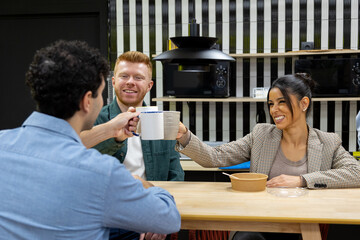 Diverse colleagues toasting mugs in modern office kitchen