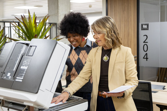 Diverse businesswomen collaborating using office multifunction printer