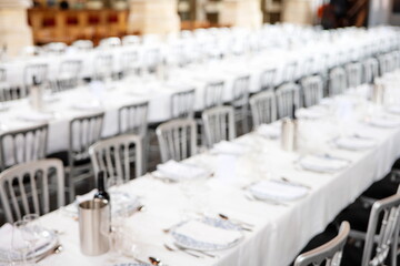 Blurry fine dinning setup of chairs, long tables with tablecloths, plates, cutlery and glasses. Wide angle, interior setting, top down, no people