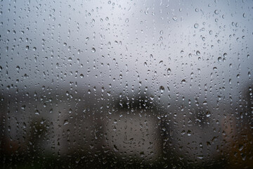 Rain drops flowing down a large home window. Close up, wide angle view, buildings in the background, no people
