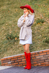 Obraz premium Portrait of a young blonde woman in a red hat and boots on an autumn walk in the city