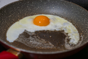 A single egg sizzles in a speckled non-stick pan, its yolk centered and glowing amid uneven whites on a warm stovetop.