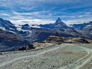 Scenic view from Gornergrat mountain towards the iconic Matterhorn peak in Switzerland. The cogwheel railway from Zermatt winds through the autumn alpine landscape.