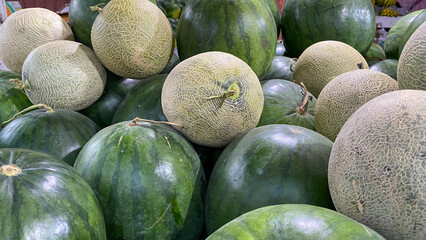 A bountiful display of whole ripe watermelons and cantaloupes piled together at a fresh fruit market stand