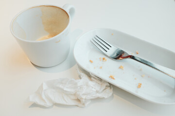 Empty cup with coffee foam, white plate with crumbs, fork, and crumpled napkin after a meal