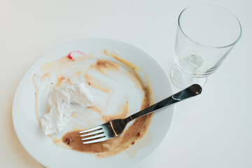 White plate with sauce smears, a crumpled napkin, and an empty glass after a finished meal on a bright table