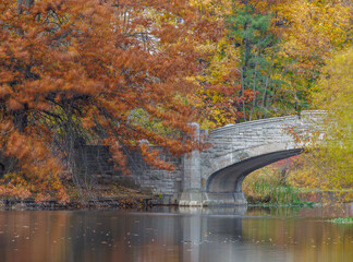A peaceful fall scene at Verona Park in New Jersey featuring a stone bridge surrounded by colorful autumn foliage reflected in calm water &mdash; a tranquil landscape full of seasonal beauty.
