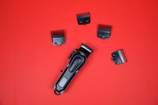 Compact electric trimmer with multiple detachable combs arranged around it on a red surface, ideal for grooming, beard shaping, and precise hair cutting. - Powered by Adobe