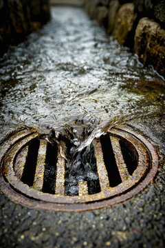 Water flowing into storm drain hatch during rain, capturing urban drainage in action