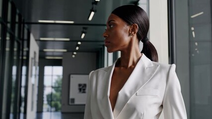Confident woman white suit walking through modern office with professional elegant hairstyle, businesswoman poised glass corridor, stylish urban