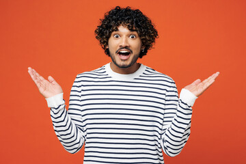 Young shocked surprised amazed impressed happy Indian man he wear striped sweatshirt casual clothes look camera spread hands isolated on plain red orange background studio portrait. Lifestyle concept.