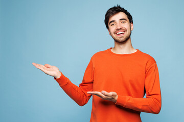 Young smiling Caucasian man he wearing orange sweatshirt casual clothes point hands arms aside...