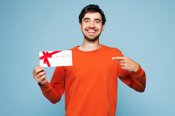 Young happy man wear orange sweatshirt casual clothes hold point finger on gift certificate coupon...