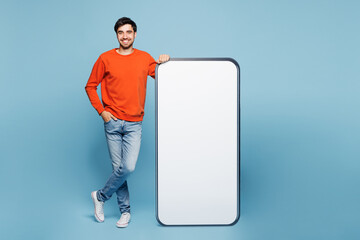 Full length young smiling fun man he wear orange sweatshirt casual clothes stand near big huge...